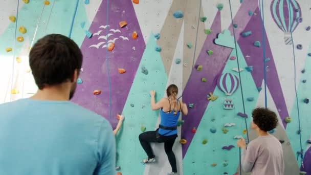 Slow motion of mother and daughter climbing wall in gym with support of belayers — Stock Video