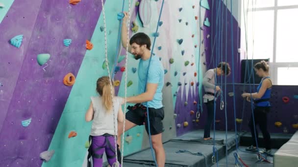 Инструктор-мужчина разговаривает с маленькой девочкой в спортзале, объясняя требования безопасности — стоковое видео
