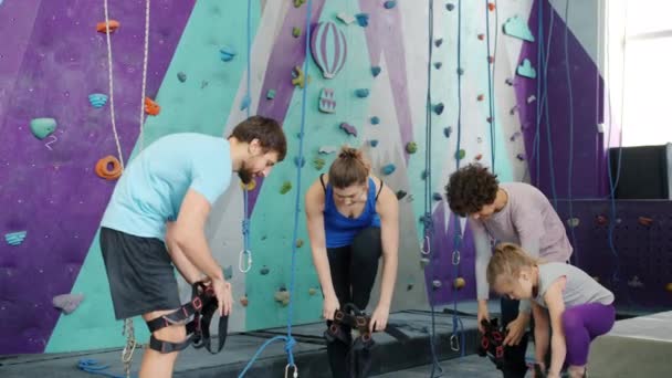 Group of young people and child putting on safety harnesses in climbing center — Stock Video