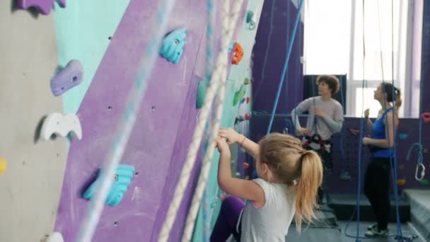 Маленькая девочка лазает по искусственной стене в скалолазании, наслаждаясь экстремальной активностью — стоковое видео