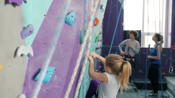 Liten flicka klättring konstgjord vägg i bergsklättring gym njuter av extrem aktivitet — Stockvideo