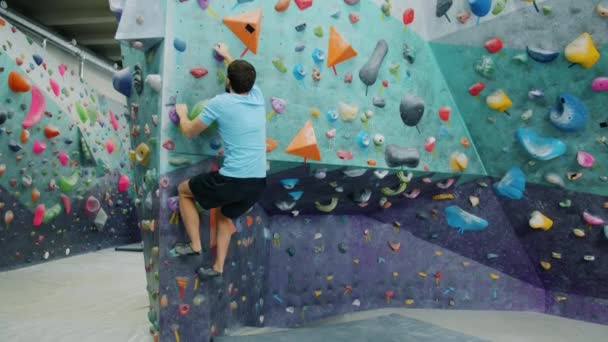 Sporty guy training in indoor climbing gym moving up wall holding artificial rocks — Stock Video