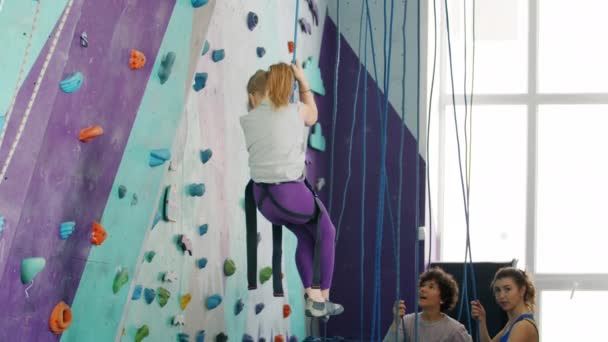 Niño feliz bajando muro de escalada artificial mientras las mujeres hablan en segundo plano — Vídeo de stock