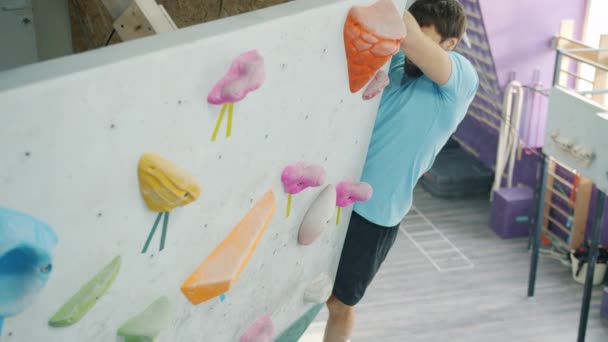 Опытный альпинист, поднимающийся по искусственной стене в спортзале, захватывает скалы в помещении — стоковое видео