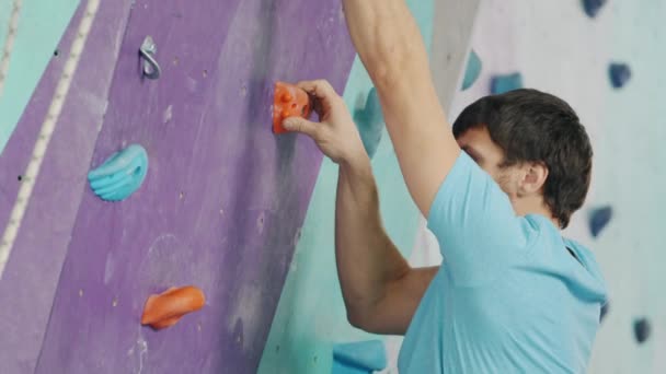 Young man climbing up artificial wall in gym wearing safety equipment — Stock Video