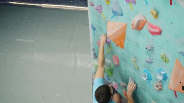 Slow motion of male climber pulling himself up on climbing wall in sports center — Stock Video