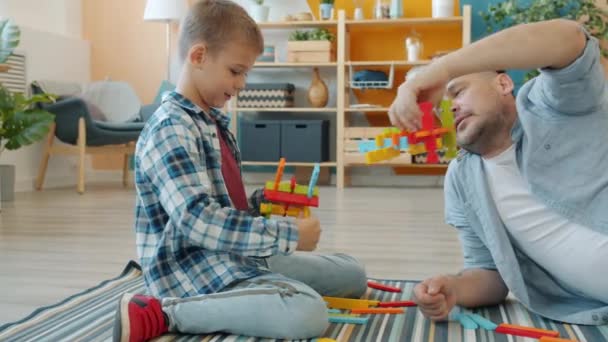 Radosny ojciec i syn bawią się drewnianymi zabawkami relaksującymi śmiejąc się w domu — Wideo stockowe
