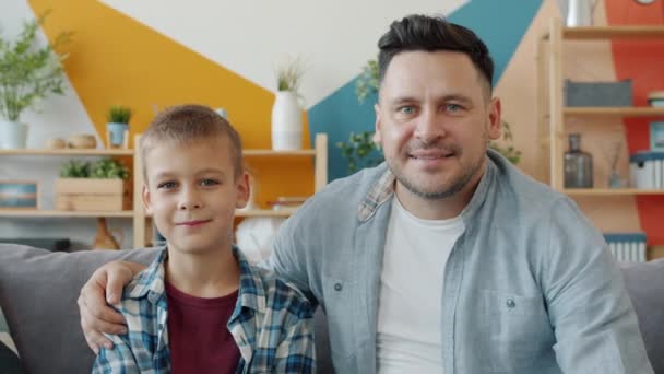 Portré két ember fiatal felnőtt apa és aranyos kisfiú mosolyog kanapén otthon — Stock videók