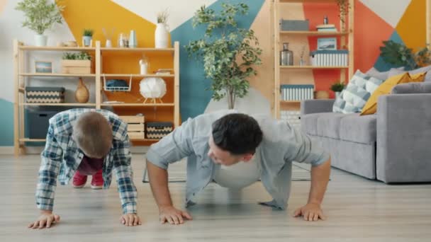 Active young man and little boy doing push-ups then doing high-five in apartment — Stock Video