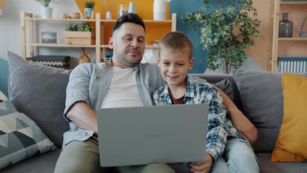 Hombre adulto y niño pequeño usando computadora portátil escribiendo mirando la pantalla y riendo en casa — Vídeos de Stock