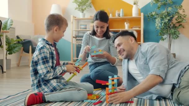 Feliz familia madre, padre e hijo jugando con juguetes de construcción en casa hablando — Vídeo de stock