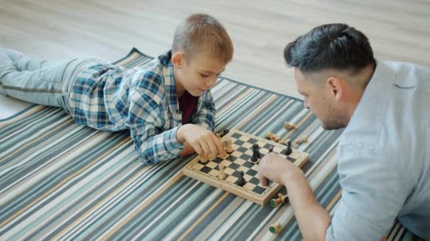 Criança inteligente jogando xadrez jogo de tabuleiro com o pai passar tempo livre em casa — Vídeo de Stock