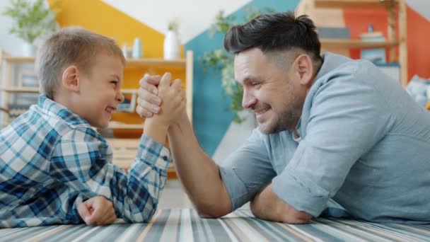 Hombre de mediana edad y niño pequeño están practicando la lucha del brazo en casa disfrutando de la actividad — Vídeo de stock