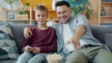 Babayla oğlunun koltukta oturup gülerken eğlenceli bir film izlemesi.
