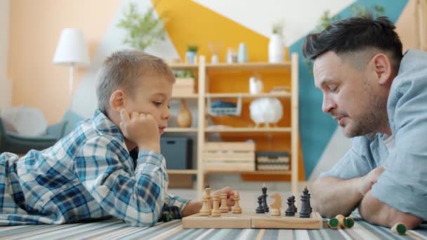 Μικρό παιδί απολαμβάνει το σκάκι παιχνίδι με φροντίδα του πατέρα ξοδεύοντας ελεύθερο χρόνο στο σπίτι — Αρχείο Βίντεο