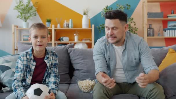 Retrato de padre e hijo viendo deportes en la televisión y luego haciendo high-five disfrutando de la victoria — Vídeo de stock