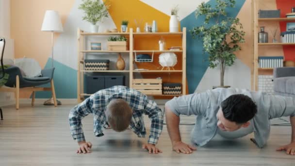 Padre e hijo haciendo ejercicio juntos haciendo flexiones en el interior del apartamento — Vídeo de stock
