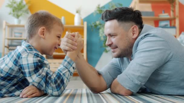 Zeitlupe: Vater und Sohn genießen zu Hause das Armdrücken auf dem Boden und lachen — Stockvideo
