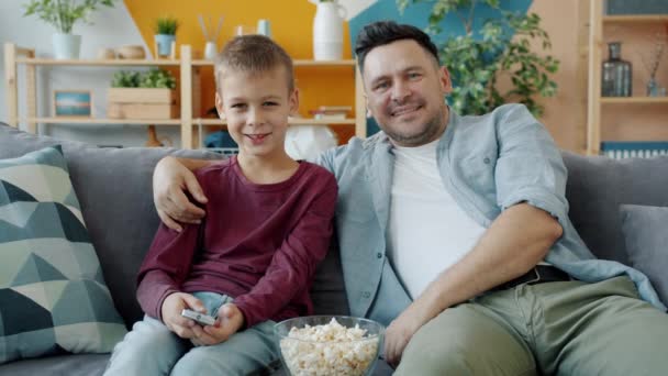 Joyful family father and son watching movie on TV eating popcorn talking in apartment — Stock Video