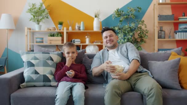 Retrato de un joven y un niño pequeño viendo la televisión en casa apuntando a la pantalla riendo — Vídeo de stock