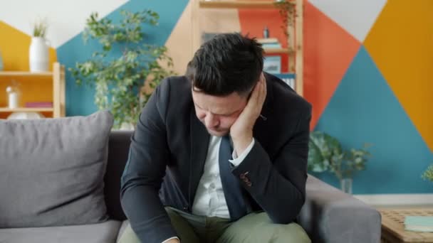 Нещасний підприємець думає про проблеми, які торкаються обличчя, сидячи на дивані вдома — стокове відео