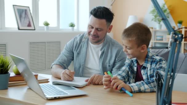Πατέρας και γιος σχέδιο μιλάμε χαμογελώντας κάθεται στο γραφείο με φορητό υπολογιστή στο σπίτι — Αρχείο Βίντεο
