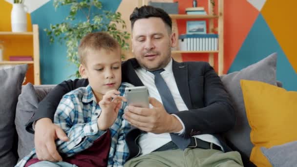 Empresario y niño pequeño usando teléfono inteligente disfrutando de contenido en línea en casa — Vídeo de stock