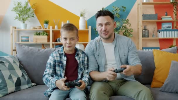 Portret van vader en kind spelen videospel thuis, knoppen indrukken op joystick praten — Stockvideo