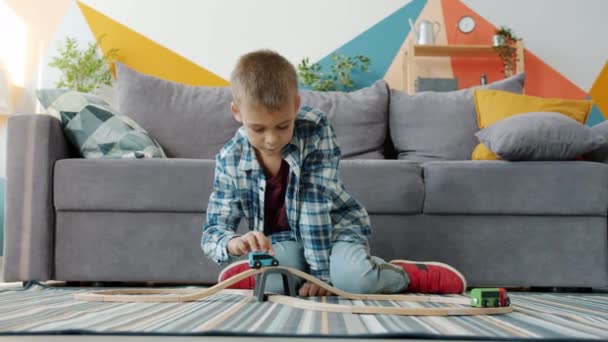 Menino despreocupado brincando com carros de brinquedo no apartamento desfrutando de jogo no chão em casa — Vídeo de Stock