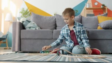Neşeli çocuk evde oyuncak arabalarla eğleniyor evde yerde tek başına oynuyor.