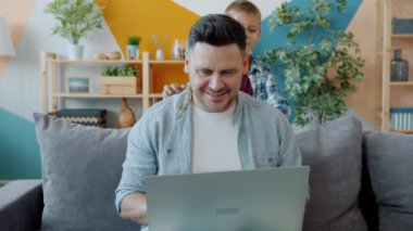 Baba dizüstü bilgisayar kullanıyor sonra da bilgisayar ekranını gösteren sevimli oğluyla konuşuyor.