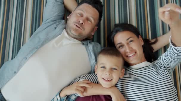 Retrato de madre, padre e hijo relajándose en el suelo en casa hablando riendo — Vídeo de stock