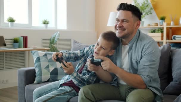 Медленное движение мужчины и мальчика, наслаждающихся видеоигрой дома, веселясь вместе — стоковое видео