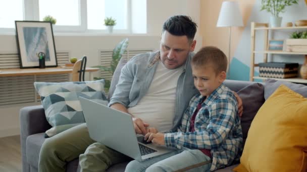 Батько і дитина грають в комп'ютерну гру, використовуючи ноутбук у квартирі, розважаючись — стокове відео