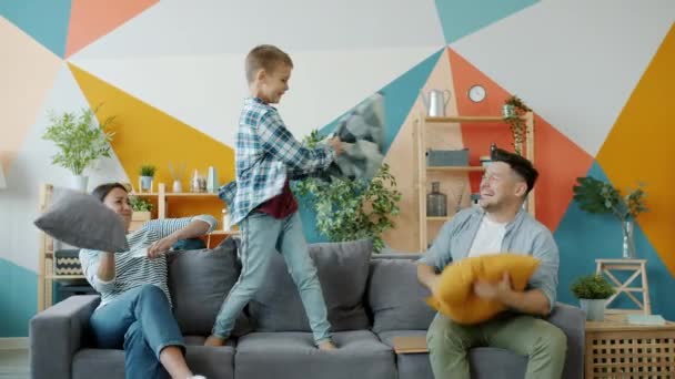Mãe, pai e criança lutando travesseiros se divertindo juntos no sofá em casa — Vídeo de Stock