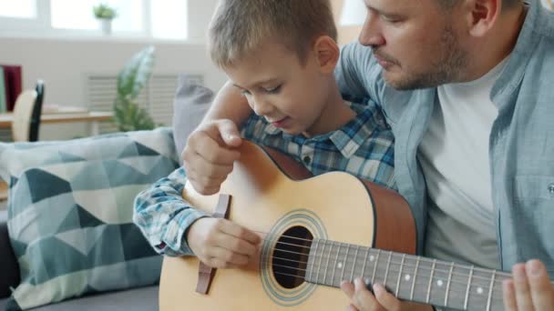 Oğluna gitar çalmayı öğreten genç bir adam evde yaratıcı aktivitelerin keyfini çıkarıyor. — Stok video