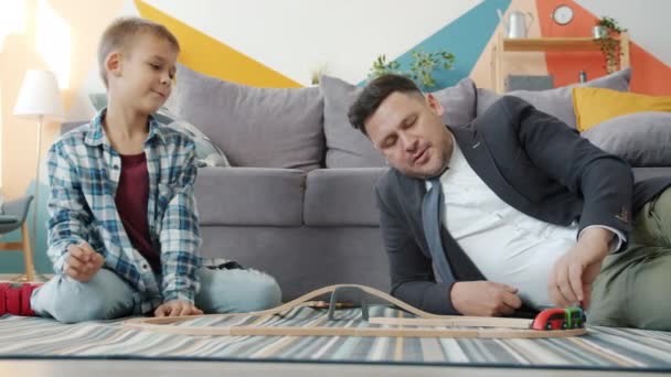 Feliz hombre de negocios jugando con lindo niño moviendo coches en el piso de divertirse — Vídeo de stock