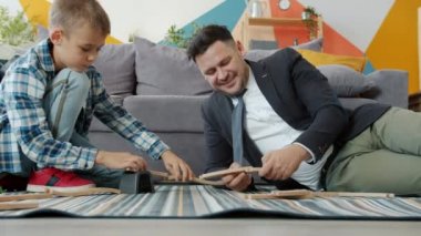 Formalite icabı giysili bir adam, sevimli bir çocukla oyuncak oynuyor. Evde ailesiyle rahatlıyor.