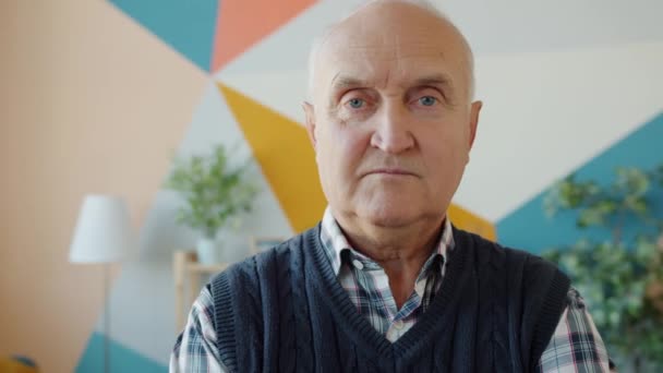Idős, ősz hajú férfi portréja, aki komoly arckifejezéssel néz a kamerába otthon — Stock videók