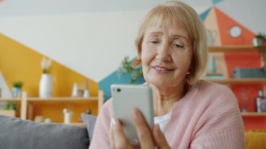 Akıllı telefon ekranından içeriği izleyen mutlu yaşlı kadının yavaş çekimi.