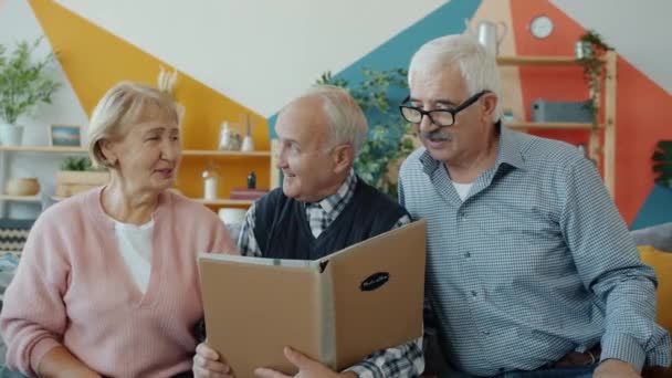 Slow motion of happy elderly people watching picture album talking laughing — Stock Video