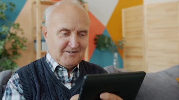 Glimlachende gepensioneerde plezier met tablet aanraken scherm ontspannen op de bank thuis — Stockvideo
