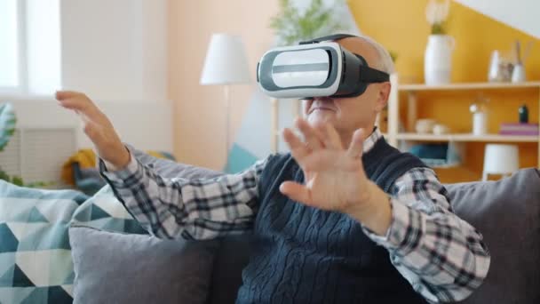 Senior man having fun with augmented reality glasses wearing headset moving hands at home — Stock Video