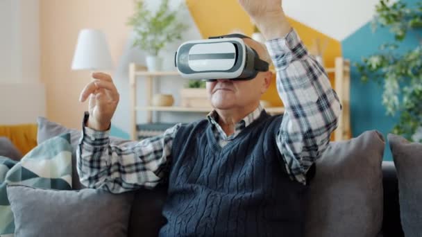 Carefree pensioner using vr glasses at home moving arms sitting on couch in apartment — Stock Video