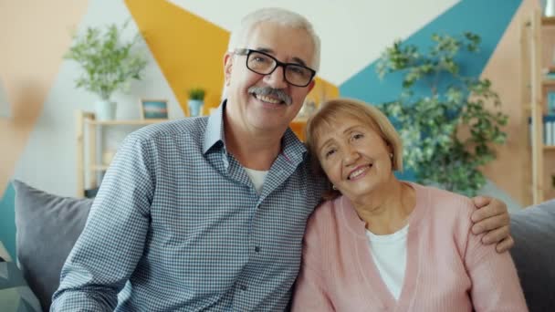 Portré idős férfi és nő pár mosolyog és nevet ül a kanapén otthon — Stock videók
