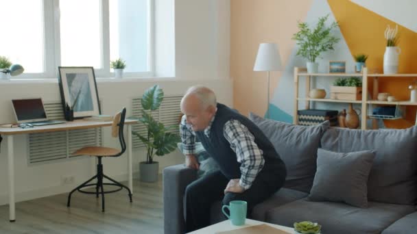 Powolny ruch seniora wstającego z sofy odczuwającego ból pleców w domu — Wideo stockowe