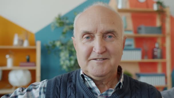 Közelkép egy nyugdíjas ősz hajú férfiról, aki otthon, fénylő mosollyal néz a kamerába. — Stock videók