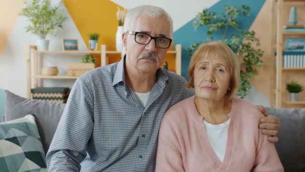 Портрет дорослої пари дорослих, яка дивиться на камеру з серйозними обличчями, що обіймаються вдома — стокове відео