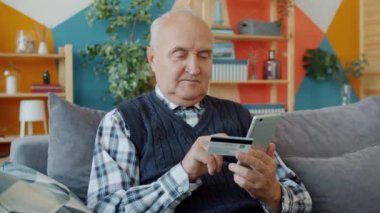 Emekli adam internetten alışveriş yapıyor. Banka kartı ve akıllı telefonla ödeme yapıyor.