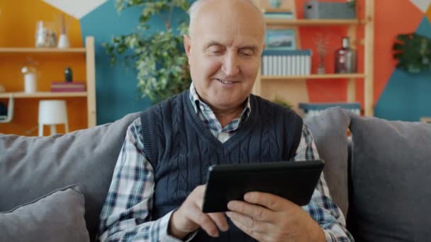 Χαρούμενος ηλικιωμένος άνδρας σαρώνει την οθόνη tablet απολαμβάνοντας το online περιεχόμενο στο σπίτι — Αρχείο Βίντεο